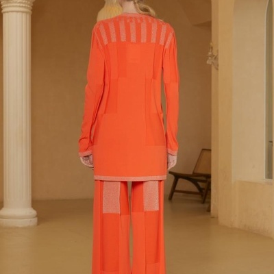 Conjunto feminino laranja de tricot com padrões geométricos, visto de costas, em ambiente interior com colunas e arcos