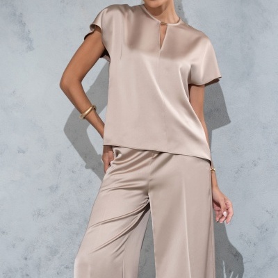 Conjunto acetinado feminino bege claro com camisa de manga curta e calças largas, em fundo cinzento