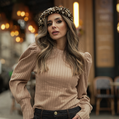 Mulher usando suéter bege com mangas bufantes e tiara preta com pérolas, em cenário urbano