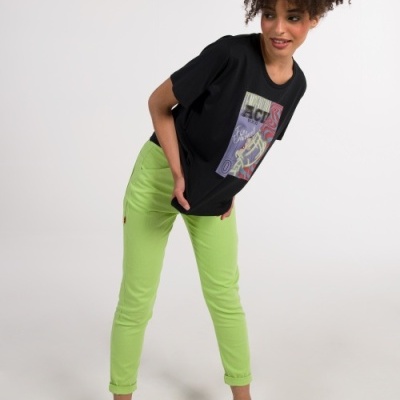 Mulher com t-shirt preta estampada, calças verde-limão e sandálias pretas