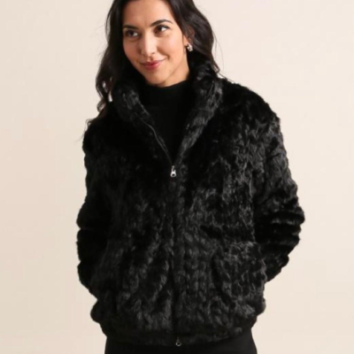 Mulher a vestir casaco preto de pele sintética com fecho de correr, em interior com parede branca