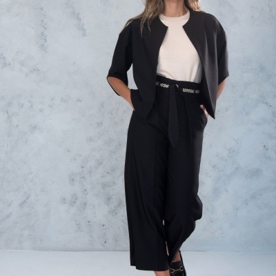 Mulher com casaco preto de manga curta, blusa branca, calças largas pretas e sapatos pretos