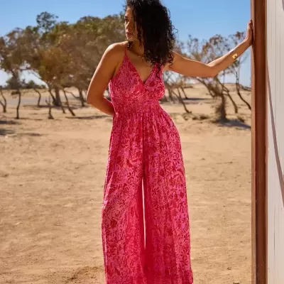 Mulher a usar macacão rosa com padrão floral em ambiente árido com árvores.