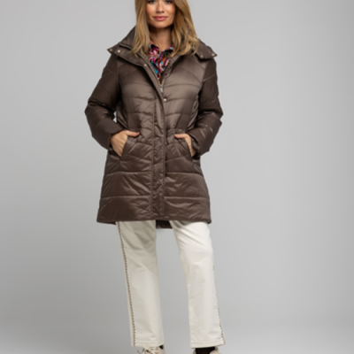 Mulher a usar casaco acolchoado castanho escuro com calças brancas e sapatos claros em fundo cinza