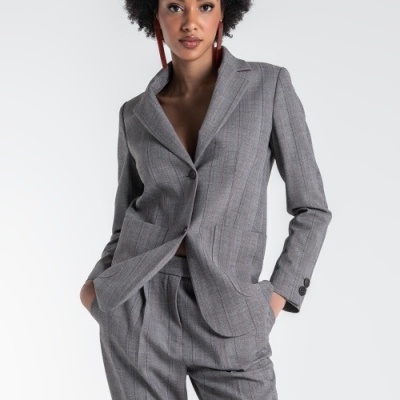 Conjunto feminino cinza padrão risca de giz com blazer e calças, modelo com brincos vermelhos, fundo branco