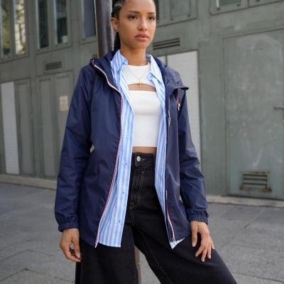 Mulher com casaco azul escuro, camisa azul riscada, top branco e calções pretos numa rua urbana