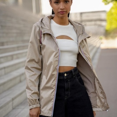 Casaco bege claro impermeável com fecho branco, camisola branca recortada e calças pretas largas num ambiente urbano