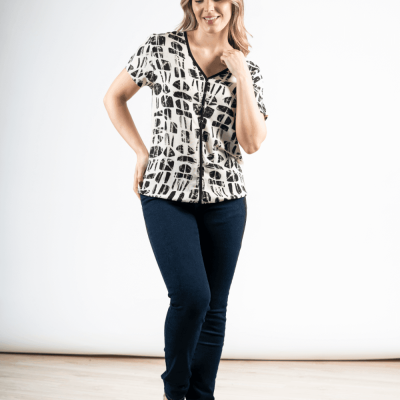 Mulher de blusa branca com padrão preto, calças azuis escuras e sandálias bege