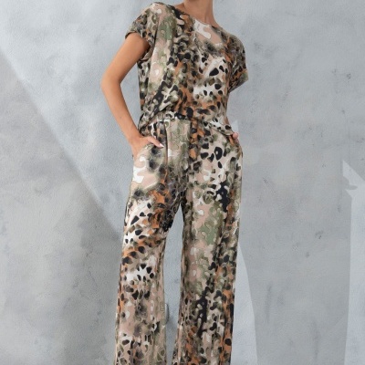 Conjunto feminino com padrão animal print verde, castanho e bege, calças largas e t-shirt, cenário parede cinzenta.
