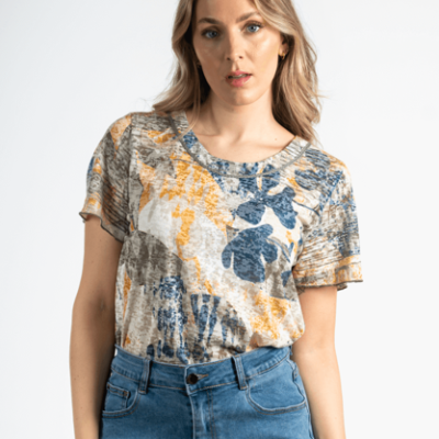 camiseta feminina com padrão abstrato azul, amarelo e cinza e calças de ganga azuis, fundo branco