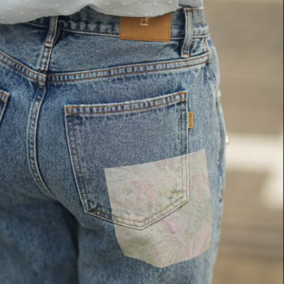 Calças de ganga azuis com bolso estampado e etiquetas visíveis, usadas por pessoa com camisa azul clara