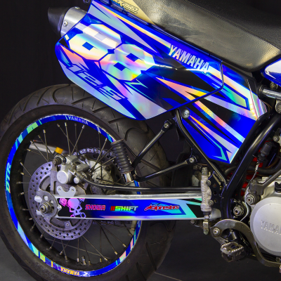 Parte traseira de motocicleta Yamaha azul com detalhes holográficos e texto na roda e braço oscilante.