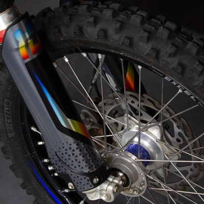 Roda dianteira de bicicleta com pneu grosso, aro azul e garfo preto com detalhes coloridos