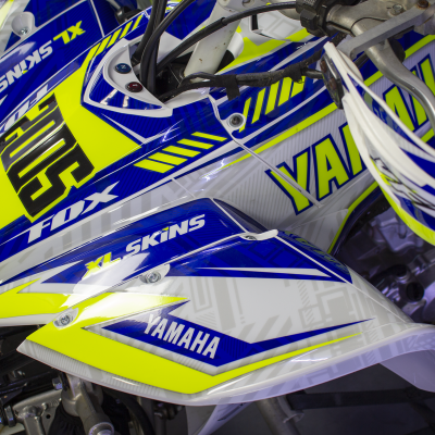 Parte da carroçaria de motocicleta Yamaha azul, amarelo e branco com textos YAMAHA, SKINS, FOX
