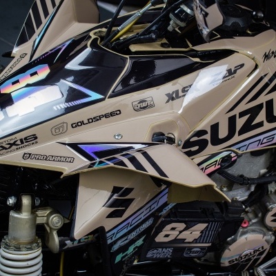 Quadri moto Suzuki creme com detalhes em preto e azul, número 84 e várias inscrições de marcas.