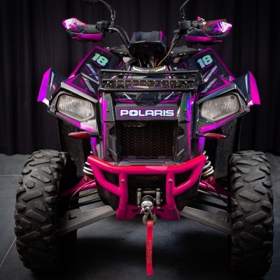 Quadriciclo Polaris rosa e roxo visto de frente com fundo escuro