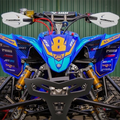 Quad ATV azul com detalhes amarelos, número 8, proteções brancas, pneus largos, porta verde ao fundo