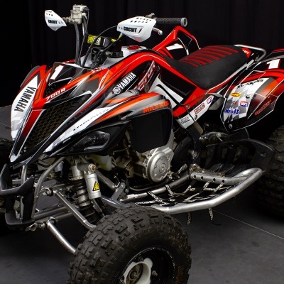 Quad Yamaha vermelho, preto e branco com texto YAMAHA e RAPTOR sobre fundo preto