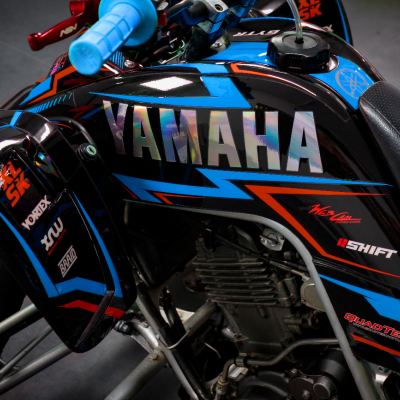 Motociclo Yamaha preto, azul e vermelho com texto refletivo YAMAHA e vários logos