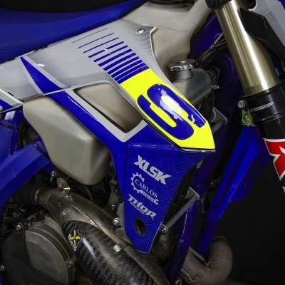 Moto de competição azul com detalhes amarelo neon e branco, e várias marcas visíveis.