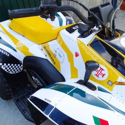 Quadriciclo branco com detalhes em amarelo, preto e verde, banco amarelo e etiquetas com texto e símbolos