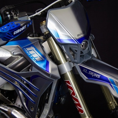 Motocicleta de competição prateada e azul com proteção azul nas mãos