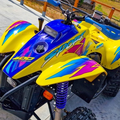 Quadriciclo amarelo colorido com texto 400 Liquid Cooled e Sport estacionado em calçada de cimento