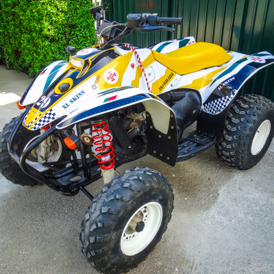 Veículo todo-o-terreno (ATV) branco, preto e amarelo com suspensão vermelha e banco amarelo.