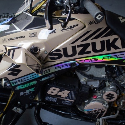 Parte lateral de mota Suzuki bege e preto com número 64 e elementos gráficos coloridos