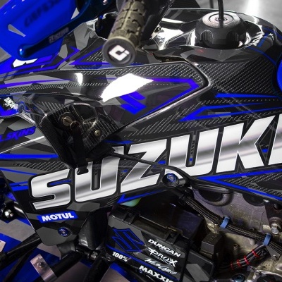 Veículo todo-o-terreno Suzuki preto e azul com detalhes em fibra de carbono e vários textos de marcas