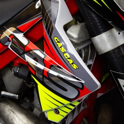 Parte de uma moto de cross com cores vermelho, preto, amarelo e branco e inscrições 'GAS GAS', 'XL' e 'SM'.