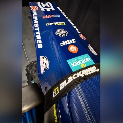 Parte de uma mota azul com vários autocolantes e logótipos visíveis