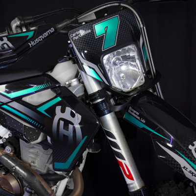 Motociclo off-road preto com detalhes em azul-turquesa e cinzento e o número 7