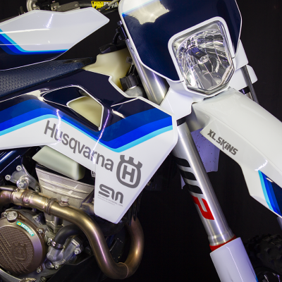 Moto de motocross Husqvarna com carenagens brancas e azuis com texto e farol dianteiro