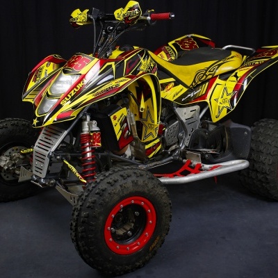 Quadriciclo amarelo com detalhes em vermelho e preto, pneus largos, suspensão vermelha e guiador com proteção