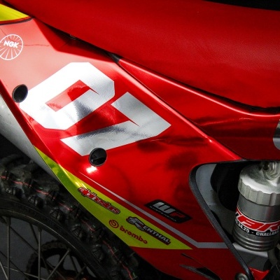 Parte traseira de mota de cross vermelha com números 07 e vários autocolantes