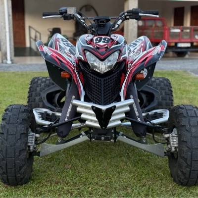 Quadriciclo vermelho preto branco com pneus largos e farol central na relva.