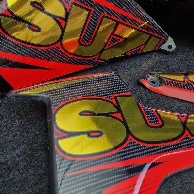 Peças em carbono para mota com letras SUZ douradas sobre fundo vermelho e preto