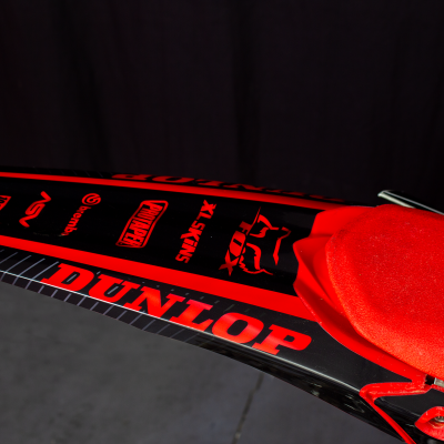 Motocicleta preto e vermelho com assento vermelho e marcas DUNLOP, PROX, VERTEX e SLS 33