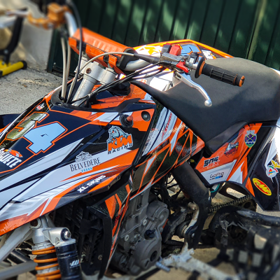 quadriciclo desportivo laranja, preto e branco com número 71 e marcas KTM e XL SKINS