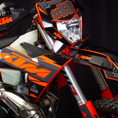 Motocross KTM laranja, preto e cinzento, número #13, etiquetas visíveis em fundo escuro
