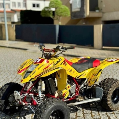 Quad Suzuki amarelo com estrutuara vermelha e pneus pretos estacionado em calçada