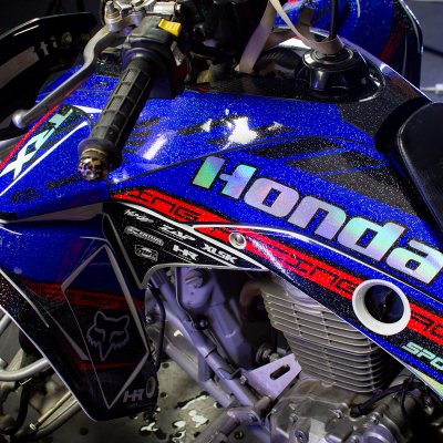 Moto todo-o-terreno azul com detalhes vermelhos, pretos e logótipos brilhantes Honda num ambiente interior