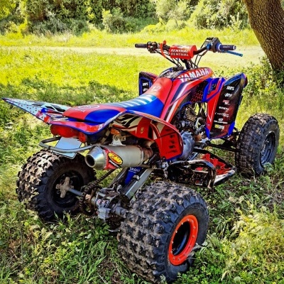 Quad Yamaha vermelho e azul em terreno com relva e árvores