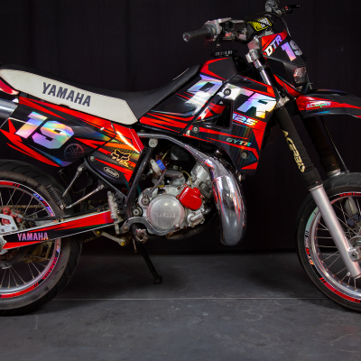 Motociclo Yamaha DT vermelho, preto e branco com números 19 em fundo escuro