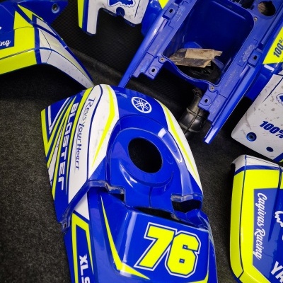 Peças plásticas azuis, amarelas e brancas para moto Yamaha com números e textos em fundo escuro.