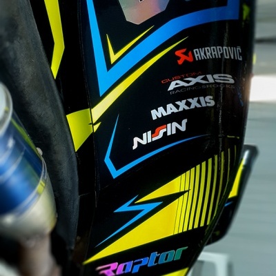 Detalhe lateral de moto de corrida com decalques e marcas visíveis.
