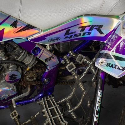 Moto todo-o-terreno com pintura branca, roxa, azul e metálica com textos LTR 450, 100%, MAXXIS