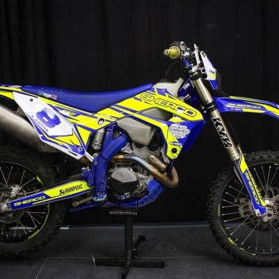 Motocross Sherco azul e amarelo com pneus de cravos e suspensão dianteira etiquetada KM3