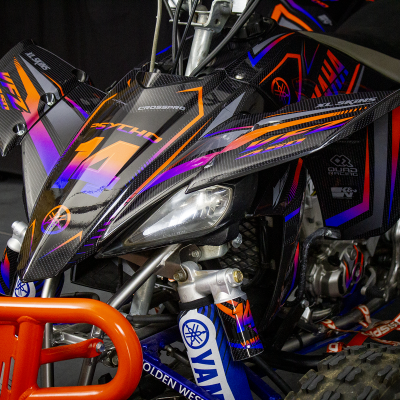 Quadriciclo preto com detalhes coloridos, para-choques laranja e suspensão azul e prateada